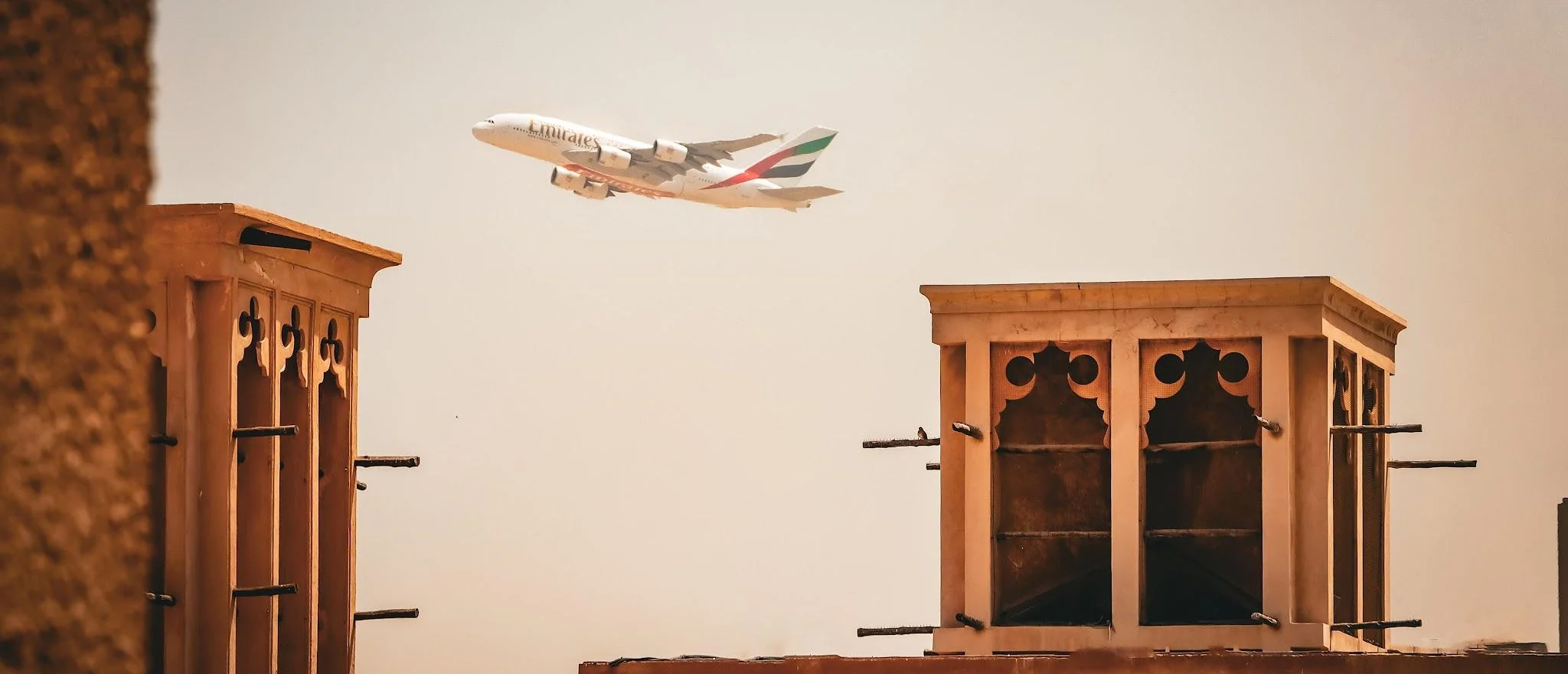 An Emirates aircraft passing above the wind towers of Al Fahidi Historical Neighbourhood in Dubai