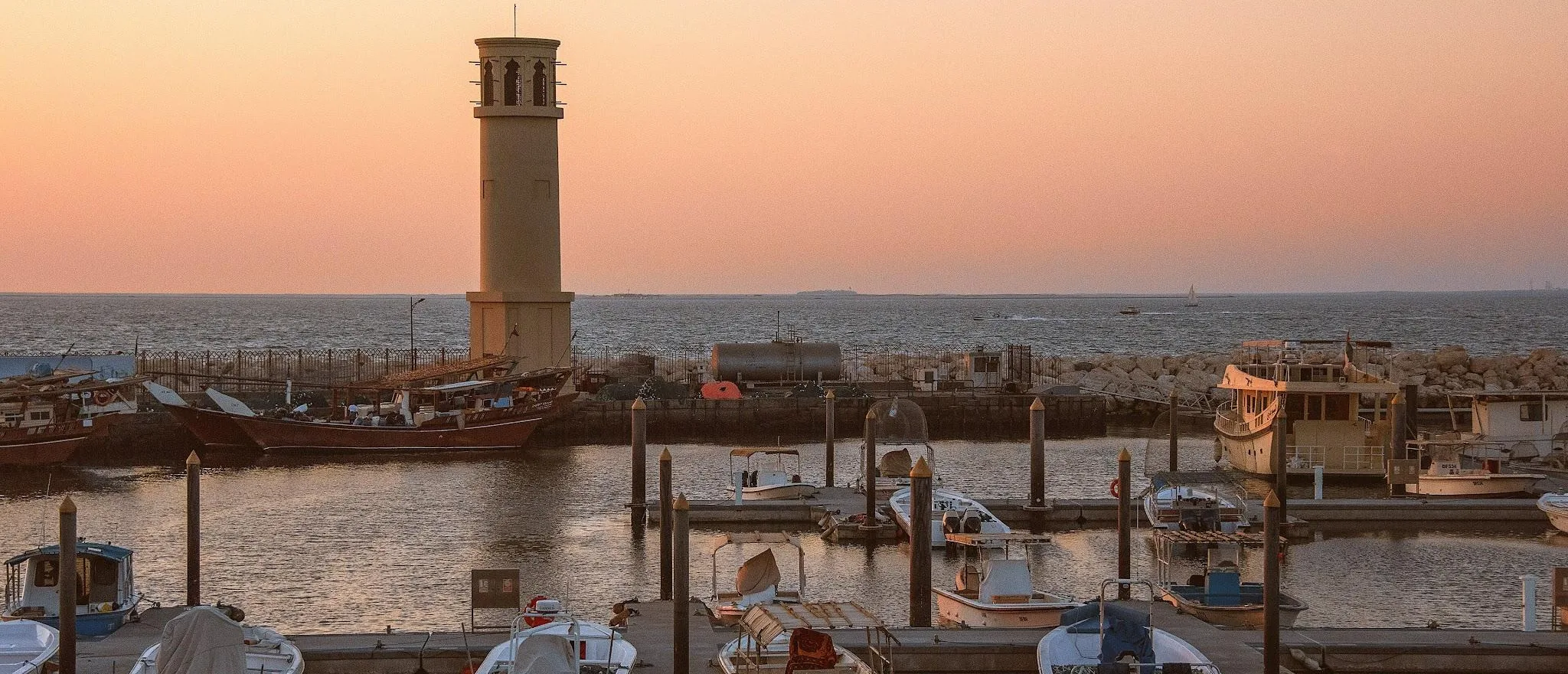 Boats and a traditional wind tower at Jumeirah harbour during sunset